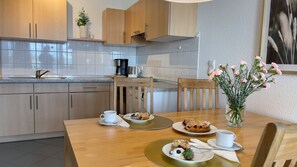A modern kitchen with wooden cabinets, a coffee maker, and a dining table set with plates of food and cups.