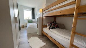 Een slaapkamer met een stapelbed, een houten ladder, een wit tapijt en een raam met gordijnen.