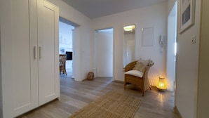 Un couloir avec un fauteuil en osier, une lampe et une porte donnant sur une pièce.