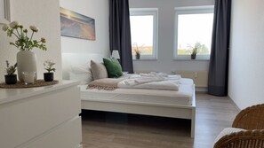 A bedroom with a bed, a nightstand, a vase with flowers, a painting, and a window with curtains.