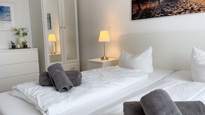 A hotel room with a bed, two bedside tables, a nightstand, a mirror, and a painting on the wall. - D1.1 - Comfortable, beautiful vacation apartment, close to the beach for up to 6 people - House (Cuxhaven)