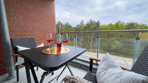A balcony with a table, two chairs, a bottle of red wine, and a glass.
