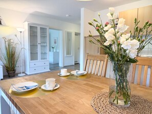 A dining area with a wooden table, white plates, a cup, and a vase with flowers.