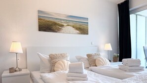 A hotel room with two beds, a painting of a beach, and a window with curtains.