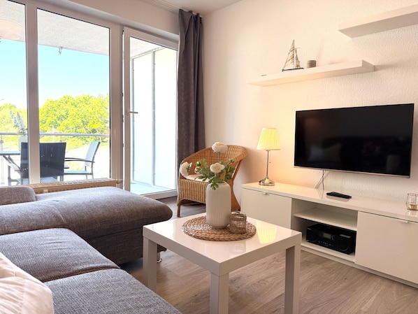 A modern living room with a sofa, a TV, and a dining area with chairs and a table.
