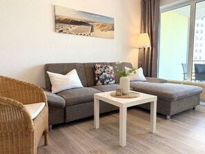 A living room with a sofa, a wicker chair, a small table with a vase, and a painting on the wall. - C1.1 - Bright, beachfront apartment with 2 balconies for up to 6 people - (Cuxhaven)
