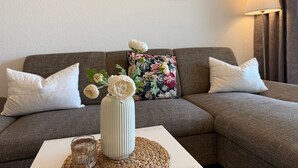 A living room with a sofa, pillows, a vase with flowers, a lamp, and a painting on the wall.