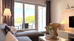 A modern living room with a sofa, a coffee table, a TV, and a balcony with outdoor furniture.