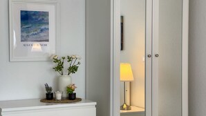 A framed artwork, a vase with flowers, a small table with a lamp, and a door.