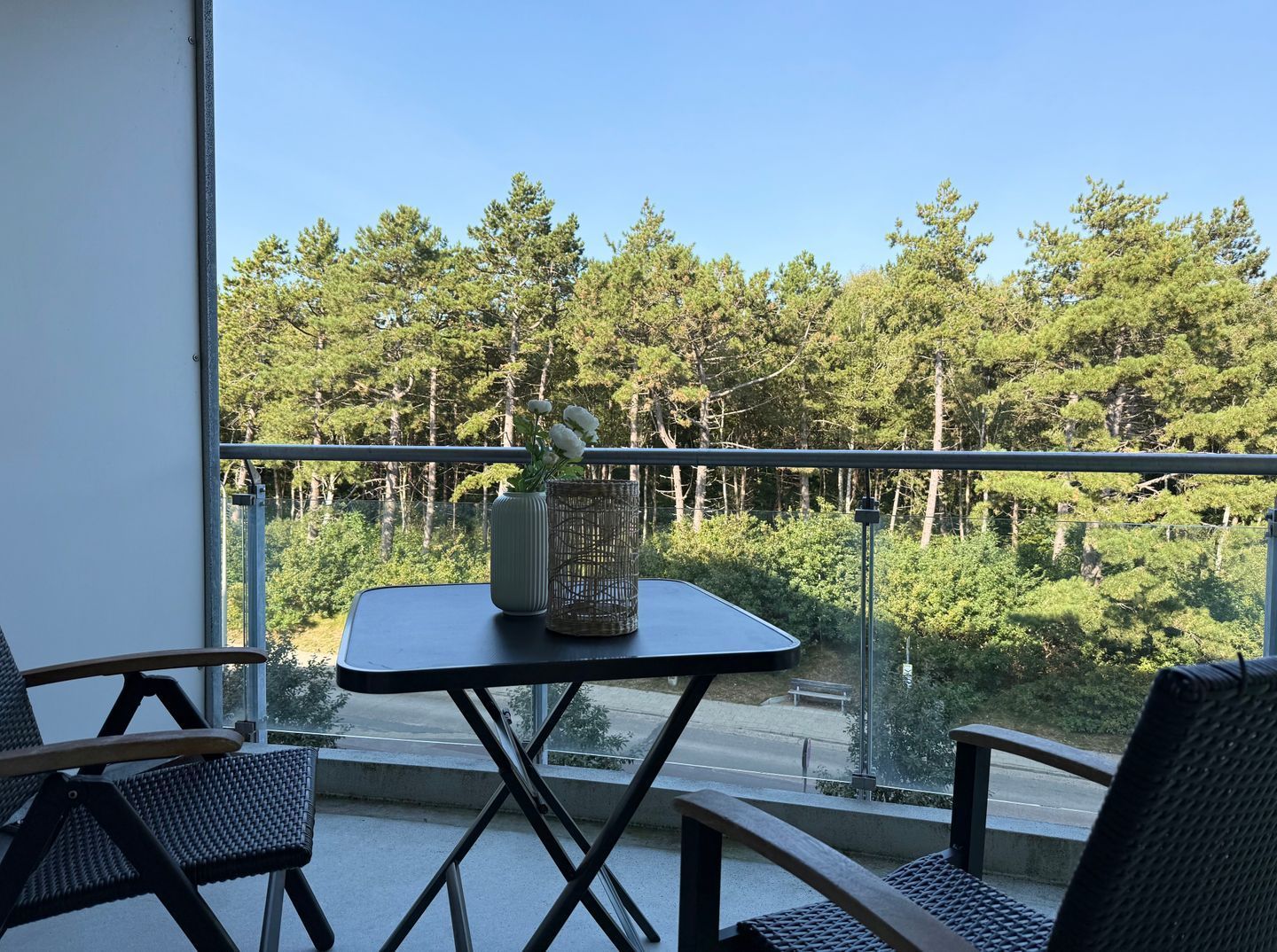 A balcony with a table and chairs, overlooking a forested area.