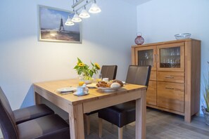 Un coin repas avec une table en bois, des chaises noires, un meuble avec des portes en verre et un tableau accroché au mur.