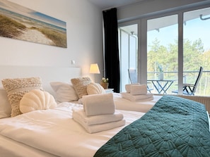Ein Hotelzimmer mit Bett, Kissen, einer grünen Steudecke, einem Fenster mit Aussicht und einem Gemälde an der Wand.