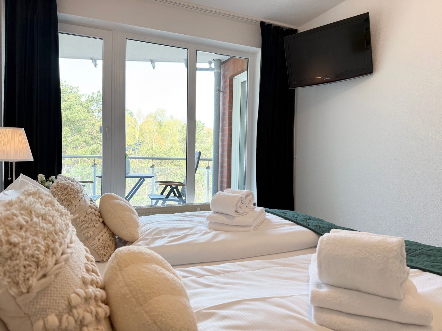 Ein Hotelzimmer mit zwei Betten, einem Flachbildfernseher und einem Balkon mit Tisch und Stühlen.
