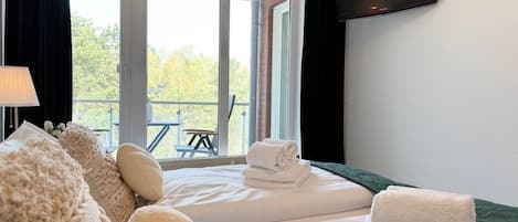 Habitación de hotel con dos camas, un televisor de pantalla plana y un balcón con mesa y sillas.