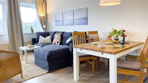 A modern living room with a sofa, dining table, chairs, and artwork on the wall.