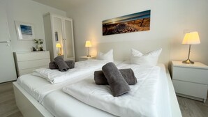 Habitación de hotel con dos camas, ropa de cama blanca, toallas grises, lámparas de noche, un cuadro en la pared y un armario blanco.