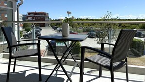 Un balcón con dos sillas, una mesa y un florero con flores.