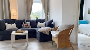 A living room with a dark blue sofa, a white coffee table, a wicker chair, and a white sofa in the background. - B2.3 - Modern apartment only 200 m from the beach, for 1-7 persons - (Cuxhaven)