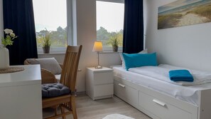 A bedroom with a bed, a chair, a nightstand, a lamp, and a window with curtains.