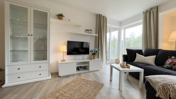 A modern living room with a flat-screen TV, white cabinetry, a black sofa, and a small white coffee table.