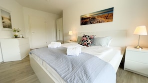 A hotel room with a large bed, a nightstand with a lamp, a painting on the wall, and a wardrobe.