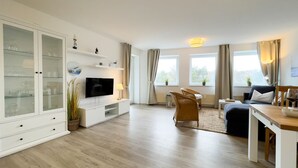 A modern living room with a flat-screen TV, a dining area with a table and chairs, a sofa, and a cabinet with glass doors. - B2.2 - Spacious, modern apartment with balcony, only 200 m to the beach - House (Cuxhaven)