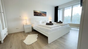 A bedroom with a large bed, bedside lamps, a white rug, and a window with a view. - B2.2 - Spacious, modern apartment with balcony, only 200 m to the beach - House (Cuxhaven)