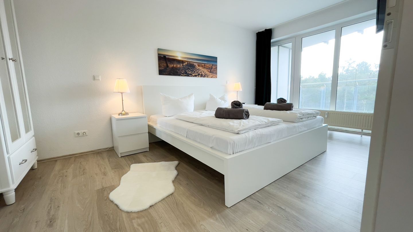 Ein Schlafzimmer mit einem großen Bett, Nachttischlampen, einem weißen Teppich und einem Fenster mit Blick.