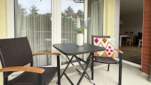 Une terrasse avec une table et des chaises, un vase rempli de fleurs et une vue à travers les portes vitrées.
