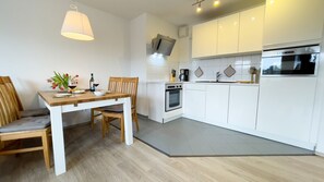 A modern kitchen with white cabinets, a dining table with chairs, and a pendant light. - B2.2 - Spacious, modern apartment with a balcony, 200 m from the beach - House (Cuxhaven)