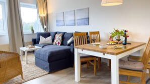 A modern living room with a sofa, dining table, chairs, and artwork on the wall. - B2.2 - Spacious, modern apartment with balcony, only 200 m to the beach - House (Cuxhaven)