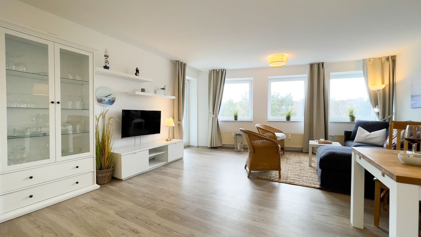 Ein modernes Wohnzimmer mit Flachbildfernseher, Essbereich mit Tisch und Stühlen, einer Couch und einem Schrank mit Glastüren.