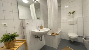 Un baño con un lavamanos blanco, un inodoro, una cortina de ducha y una planta en maceta.