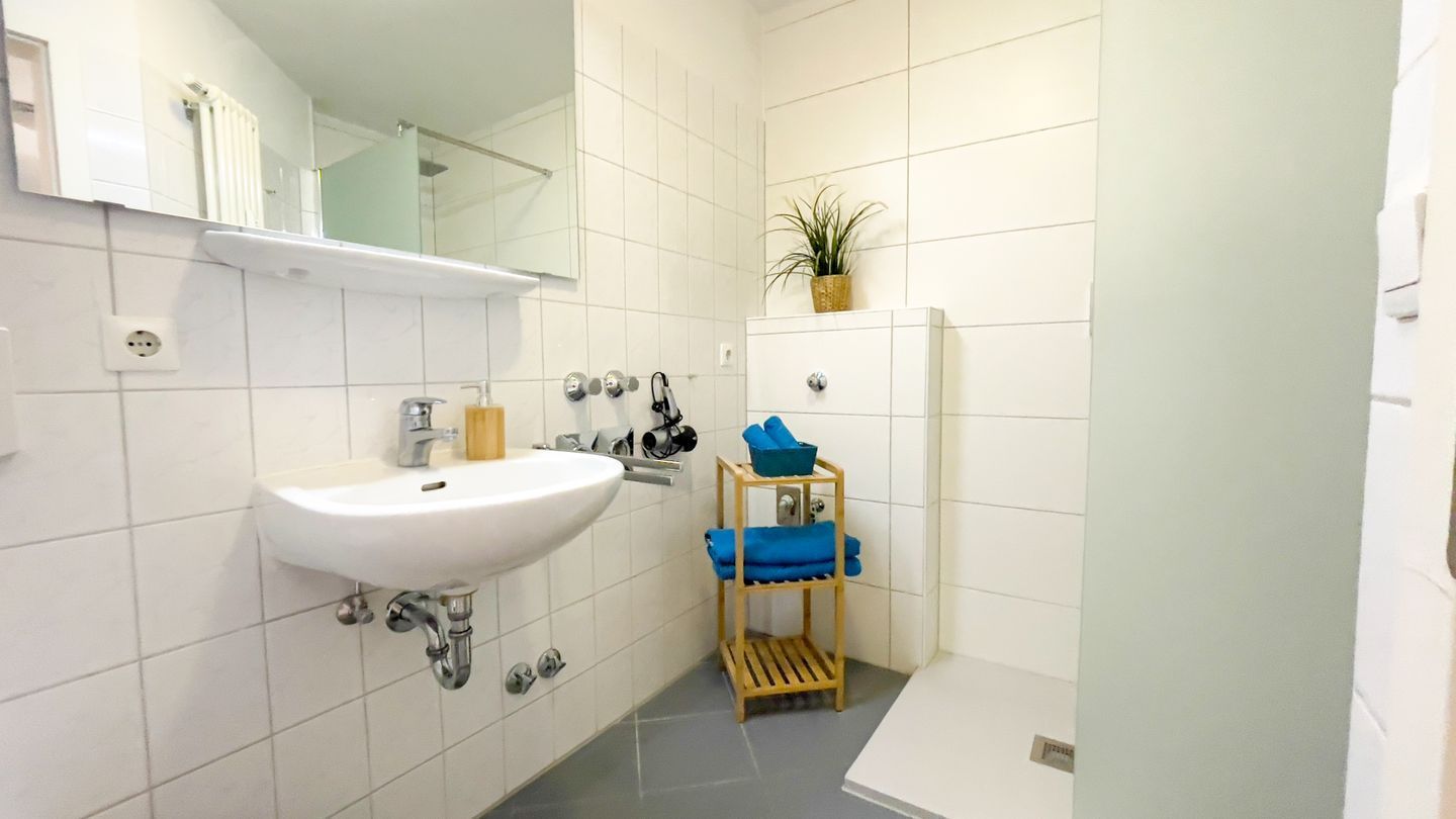 Une salle de bain avec un lavabo blanc, un miroir et une étagère où sont posées des serviettes.