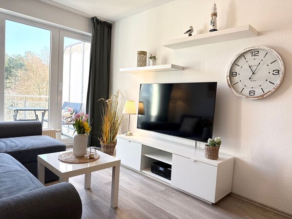 A modern living room with a flat-screen TV, a white console table, a grey sofa, and a large wall clock.