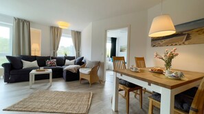 A modern living room with a sofa, a dining table, and a chair. There is a lamp on the table and a painting on the wall.