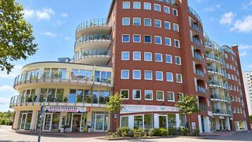 Ein mehrstöckiges Gebäude mit einer geschwungenen Fassade, Balkonen und Gewerbeflächen im Erdgeschoss.