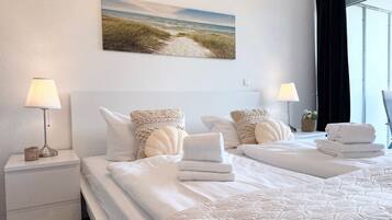 Ein Hotelzimmer mit zwei Betten, einem Strandgemälde und einem mit Vorhängen versehenen Fenster.