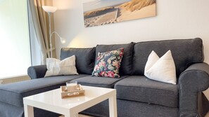 A grey sofa with white and floral cushions, a white side table with a tray of items, and a lamp. - B1.1 - Stunning beachfront apartment for 6 people - House (Cuxhaven)