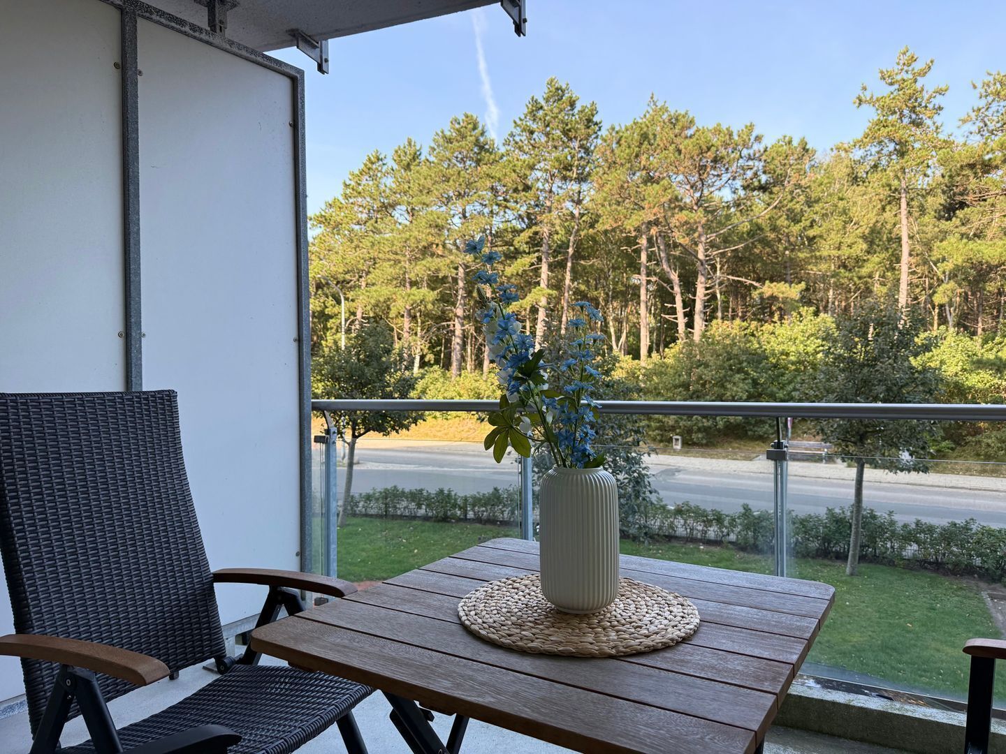 Een balkon met rieten stoelen, een houten tafel en een vaas met bloemen.