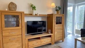 Un meuble de rangement en bois pour appareils multimédias, comprenant un téléviseur à écran plat, des meubles avec des portes en verre et une lampe.