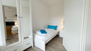 A bedroom with a bed, a wardrobe, a bedside table, and a lamp. - A4.3 - Bright and inviting apartment with a partial ocean view, for 7 people (Cuxhaven)