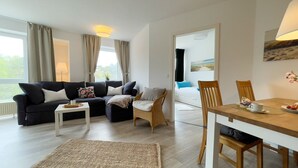 A modern living room with a sofa, coffee table, dining table, and chairs. - A4.3-Bright, friendly apartment with partial sea view, for up to 7 people (Cuxhaven)