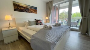 A hotel room with a bed, two bedside lamps, a painting on the wall, and a balcony with a table and chairs. - A4.3-Bright, friendly apartment with partial sea view, for up to 7 people (Cuxhaven)