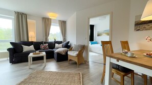 A modern living room with a sofa, coffee table, dining table, and chairs. - A4.3 - Bright and inviting apartment with a partial ocean view, for 7 people (Cuxhaven)