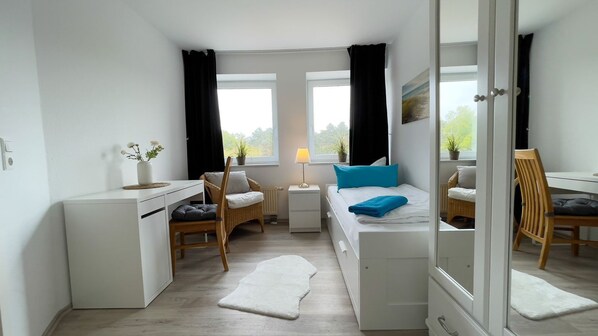 Une chambre à coucher comprenant un lit, une table de chevet, une chaise, un bureau et une fenêtre avec des rideaux.