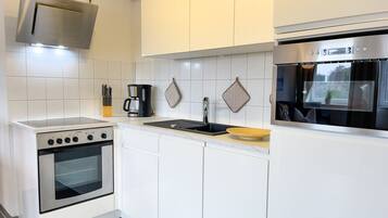 Eine moderne Küche mit weißen Schränken, einem eingebauten Backofen, einer Kaffeemaschine und einem Fenster mit Blick auf einen Garten.