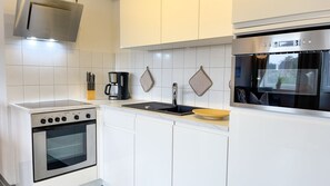 A modern kitchen with white cabinetry, a built-in oven, a coffee maker, and a window overlooking a garden.
