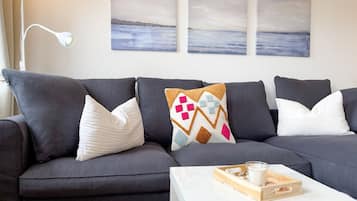 Ein dunkelgraues Sofa mit gemusterten Kissen, eine weiße Lampe und ein Tablett mit einem Glas Milch auf einem weißen Tisch.