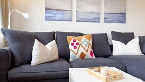 A dark grey sofa with patterned cushions, a white lamp, and a tray with a glass of milk on a white table.